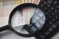 Banknoty euro, kalkulator i lupa symbolizujące analizę finansową przy obliczaniu alimentów.