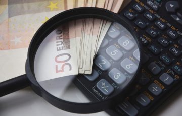 Banknoty euro, kalkulator i lupa symbolizujące analizę finansową przy obliczaniu alimentów.